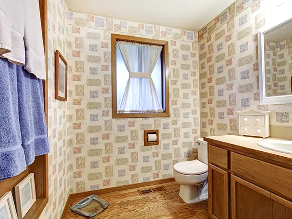Older bathroom with outdated wallpaper and wooden vanity