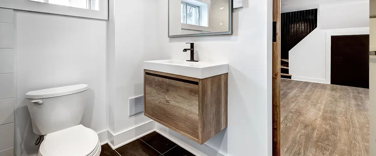 A basement with LVP flooring with a bathroom with black tile flooring and a small modern vanity