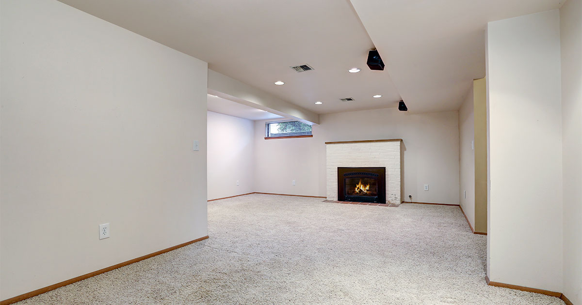 Carpet flooring in a basement with a fireplace and white walls