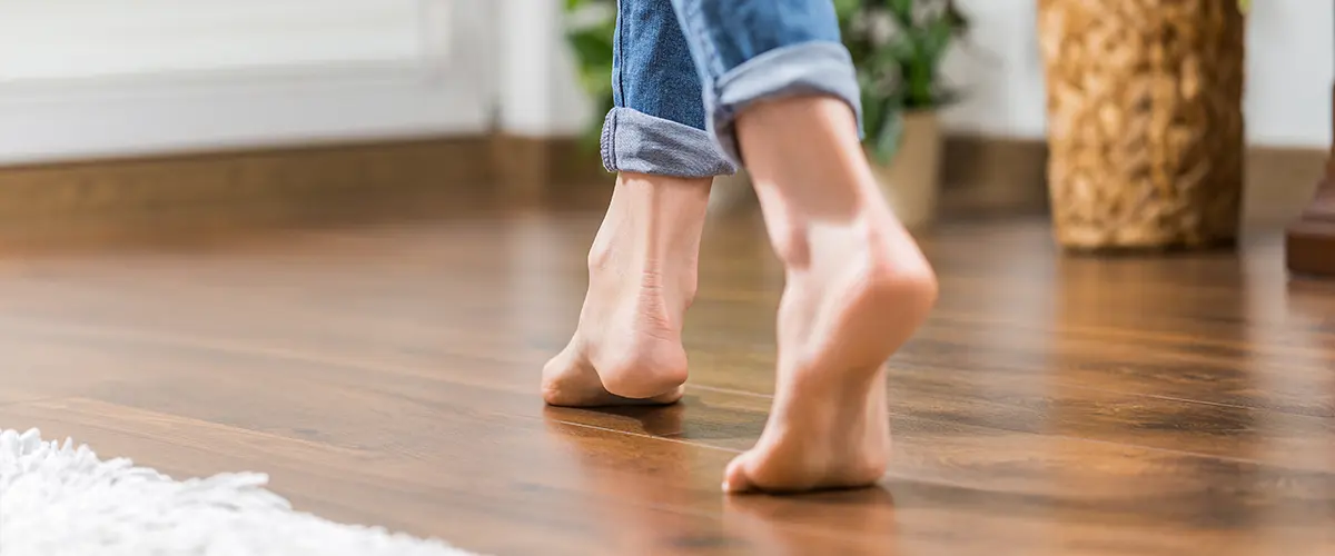 An image of a person's feet walking on a hardwood floor.