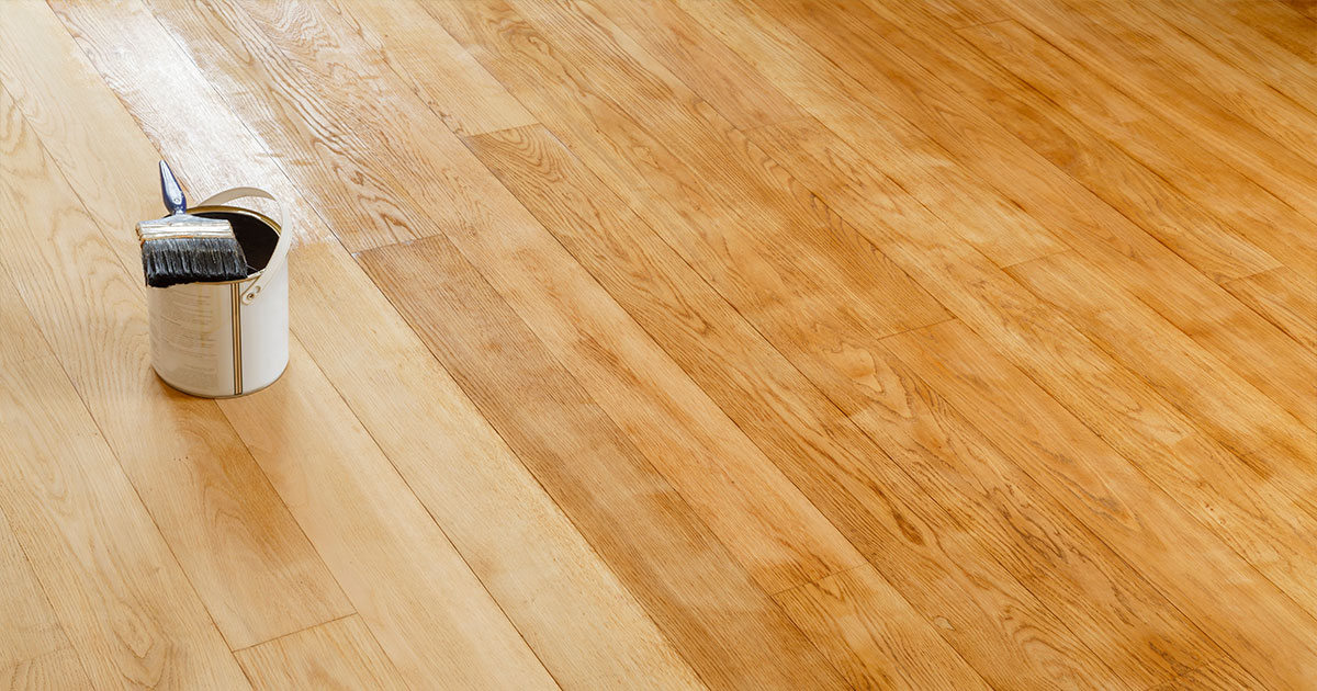 Can of stain on a hardwood floor partially staned.