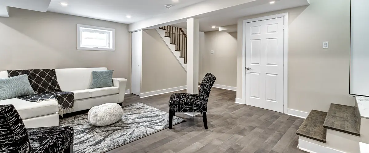 Basement living area remodeling in Florence, with modern furniture, neutral colors, hardwood floors, recessed lighting, and staircase leading upstairs.