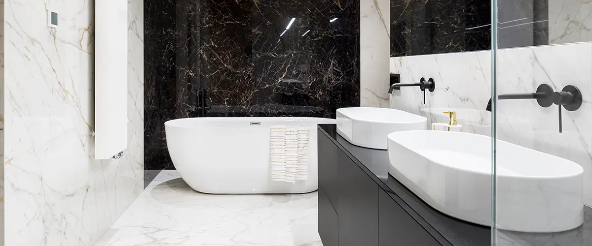 Modern bathroom with marble and dark stone tiles, featuring a freestanding bathtub and dual sinks