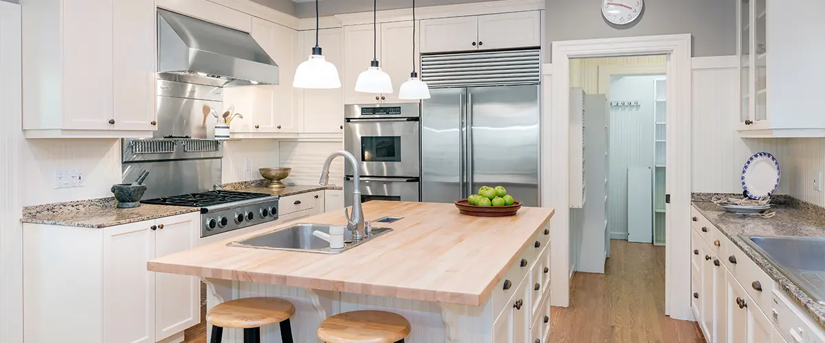 Modern remodeled kitchen in Florence, with white cabinetry, stainless steel appliances, a large central island with wooden countertop, pendant lighting, and a walk-in pantry.