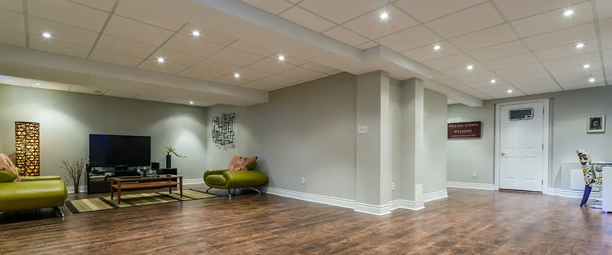 Spacious remodeled basement in Florence, with wood flooring, recessed lighting, modern green furniture, and a large flat-screen TV in an entertainment area.