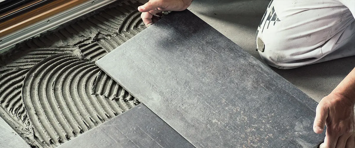 Worker placing dark grey ceramic floor tiles on adhesive surface