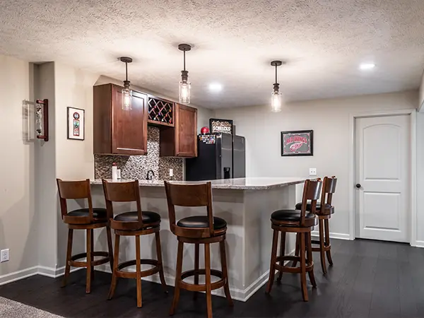 Modern basement bar with wooden stools, pendant lighting, and a granite countertop for home entertainment.