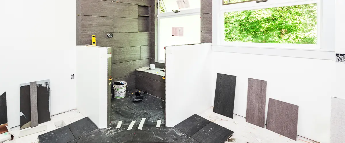 Bathroom renovation in progress with gray tile installation and unfinished flooring