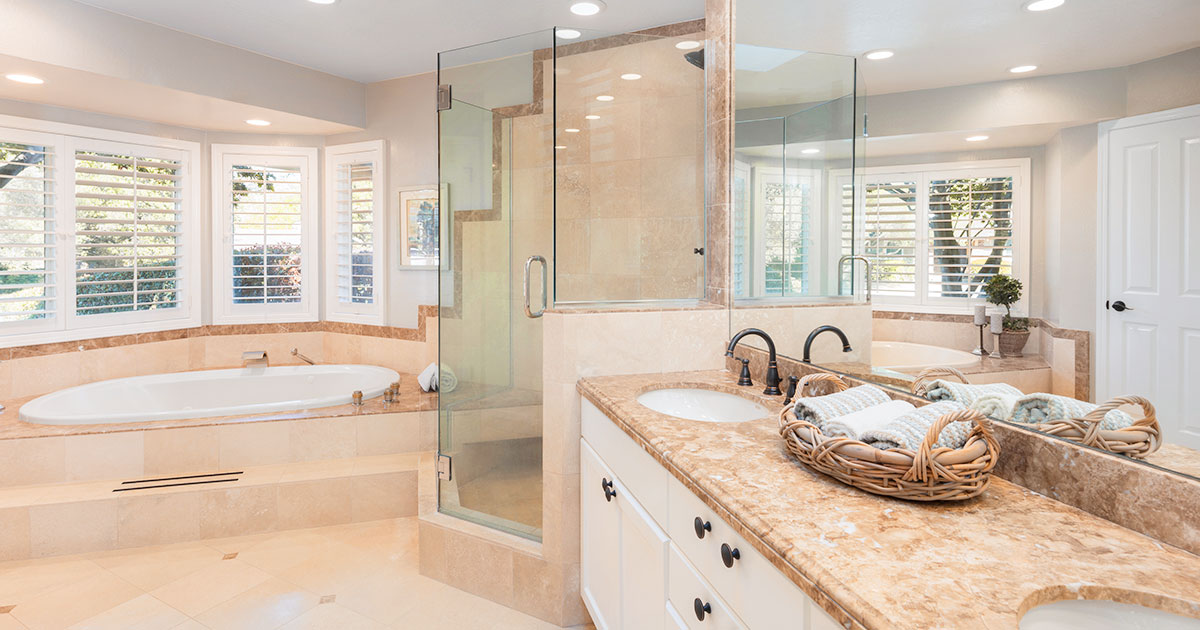 Spacious bathroom with glass shower, marble countertops, soaking tub, and large windows with shutters