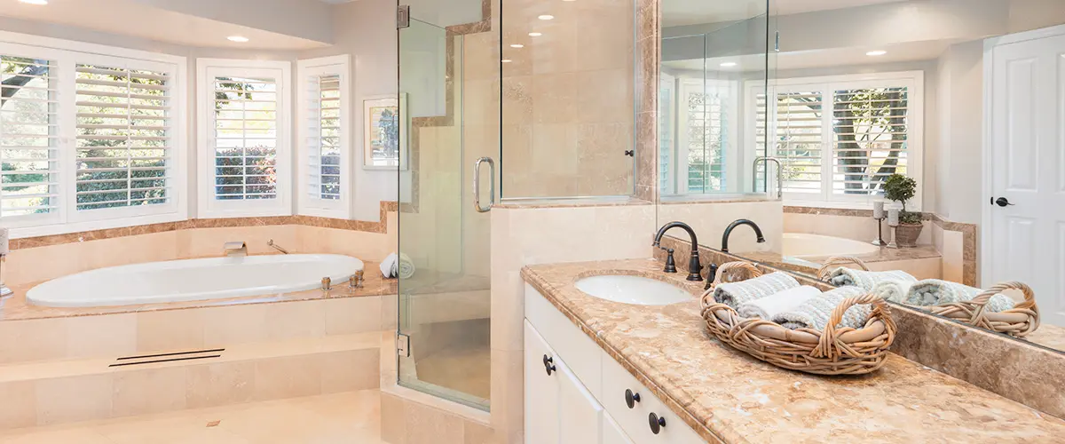 Spacious bathroom with glass shower, marble countertops, soaking tub, and large windows with shutters