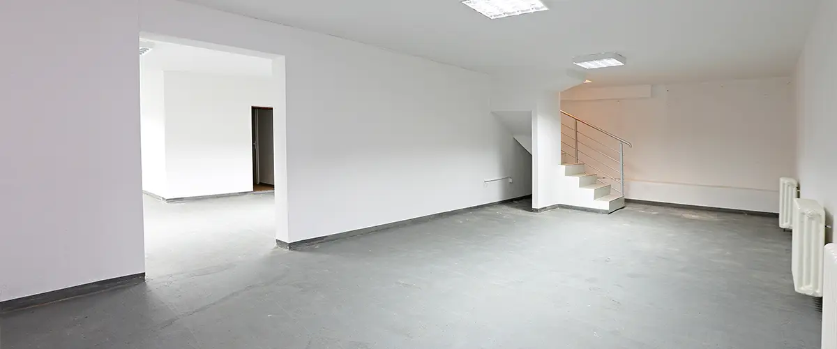 Unfinished basement with concrete floor, white walls, and staircase - empty space for renovation or remodeling project.