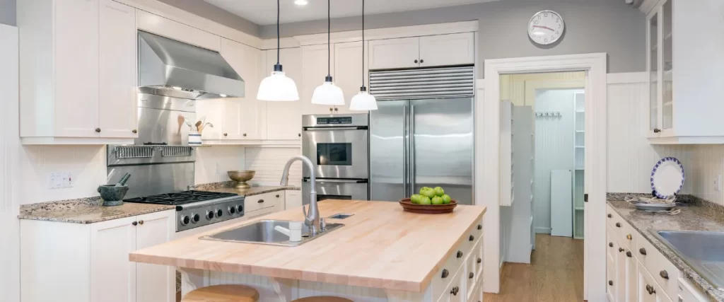 Alternate angle of classic white kitchen with pendant lighting and green apples on the island