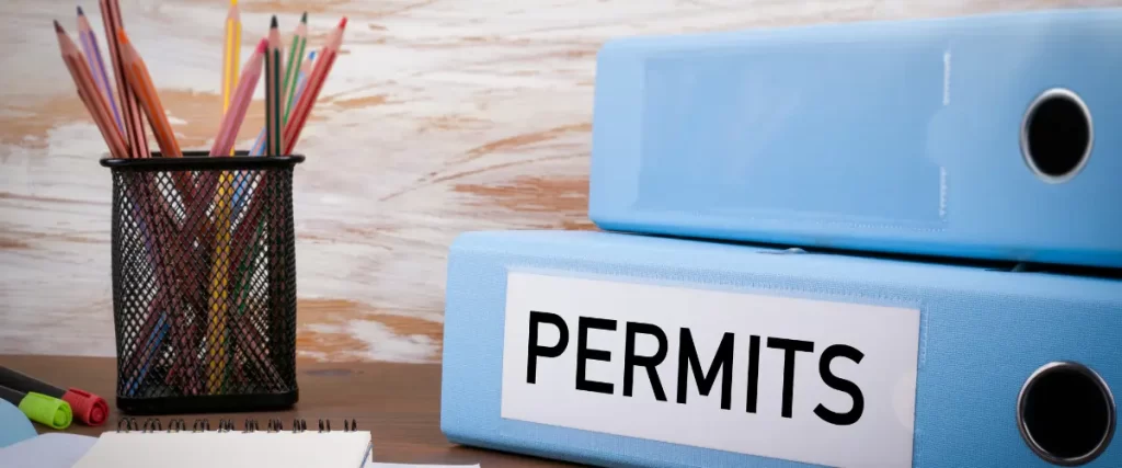 Blue binder labeled 'Permits' on a desk with colored pencils and papers